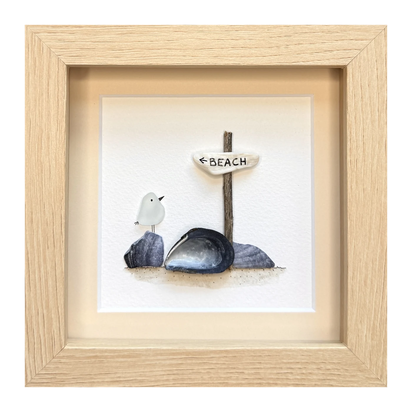 A white sea glass bird beside a mussel shell and stones, under a driftwood beach sign