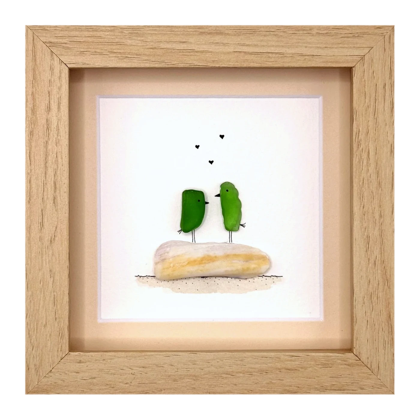 Two green sea glass birds on a pale stone with hearts