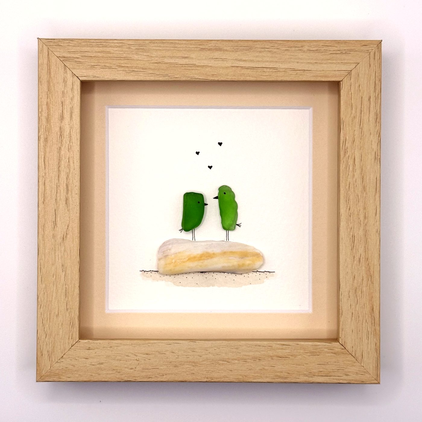 Two green sea glass birds on a pale stone with hearts